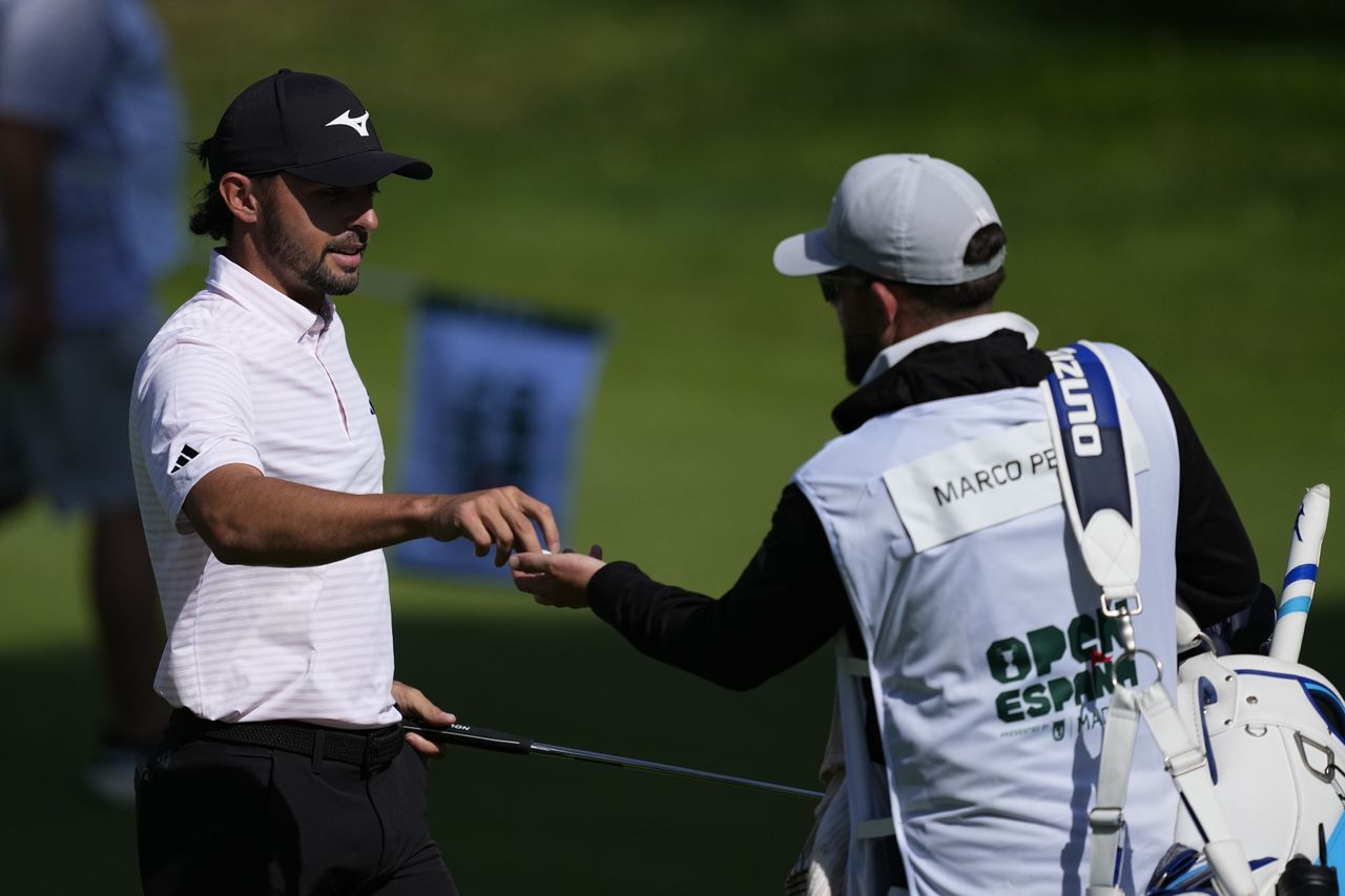 Marco Penge hands a golf ball over to his caddie