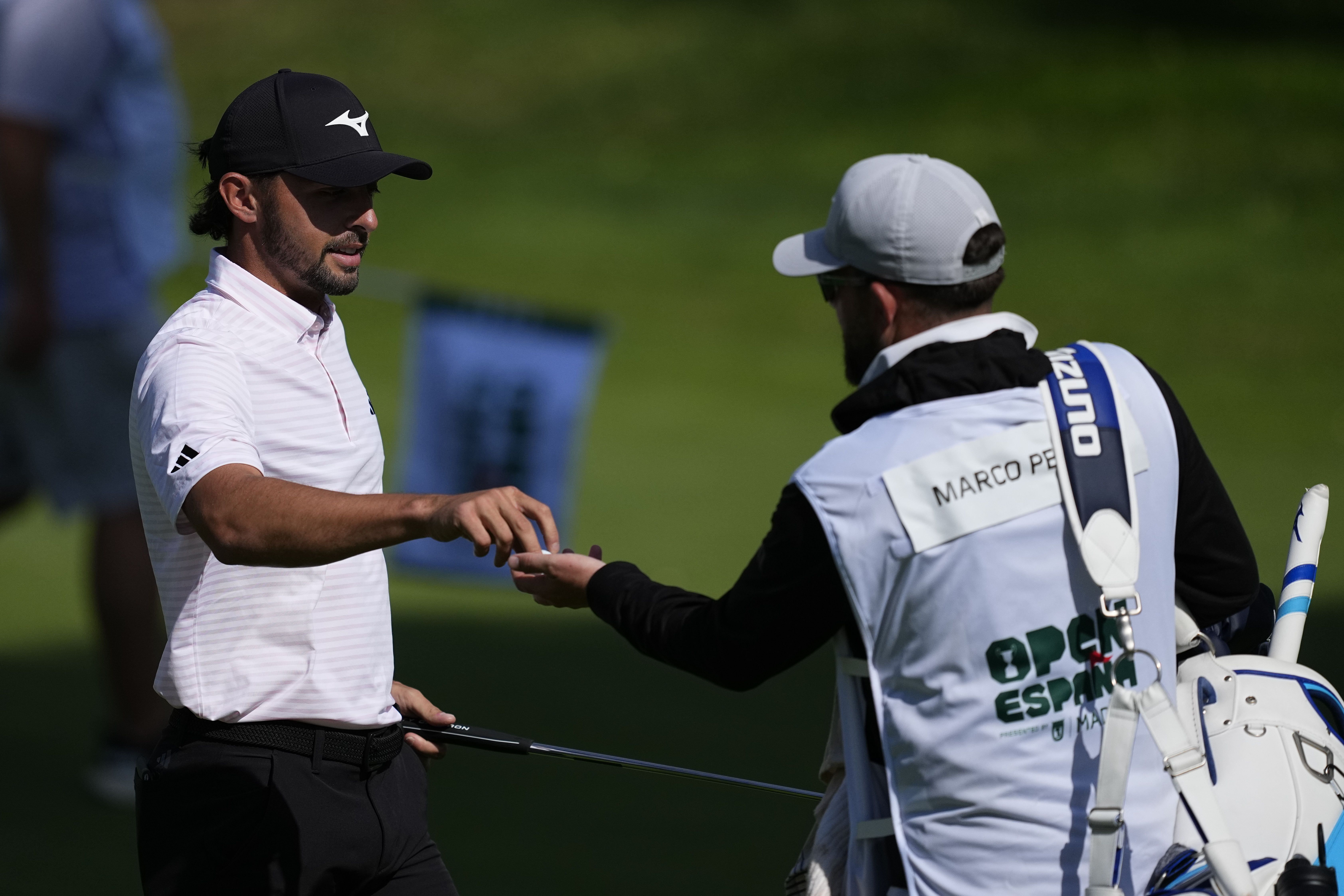 Marco Penge hands a golf ball over to his caddie