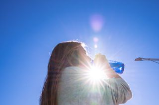 Blonde woman drinking water outside while being illuminated by a ray of sunlight during a level 4 heatwave