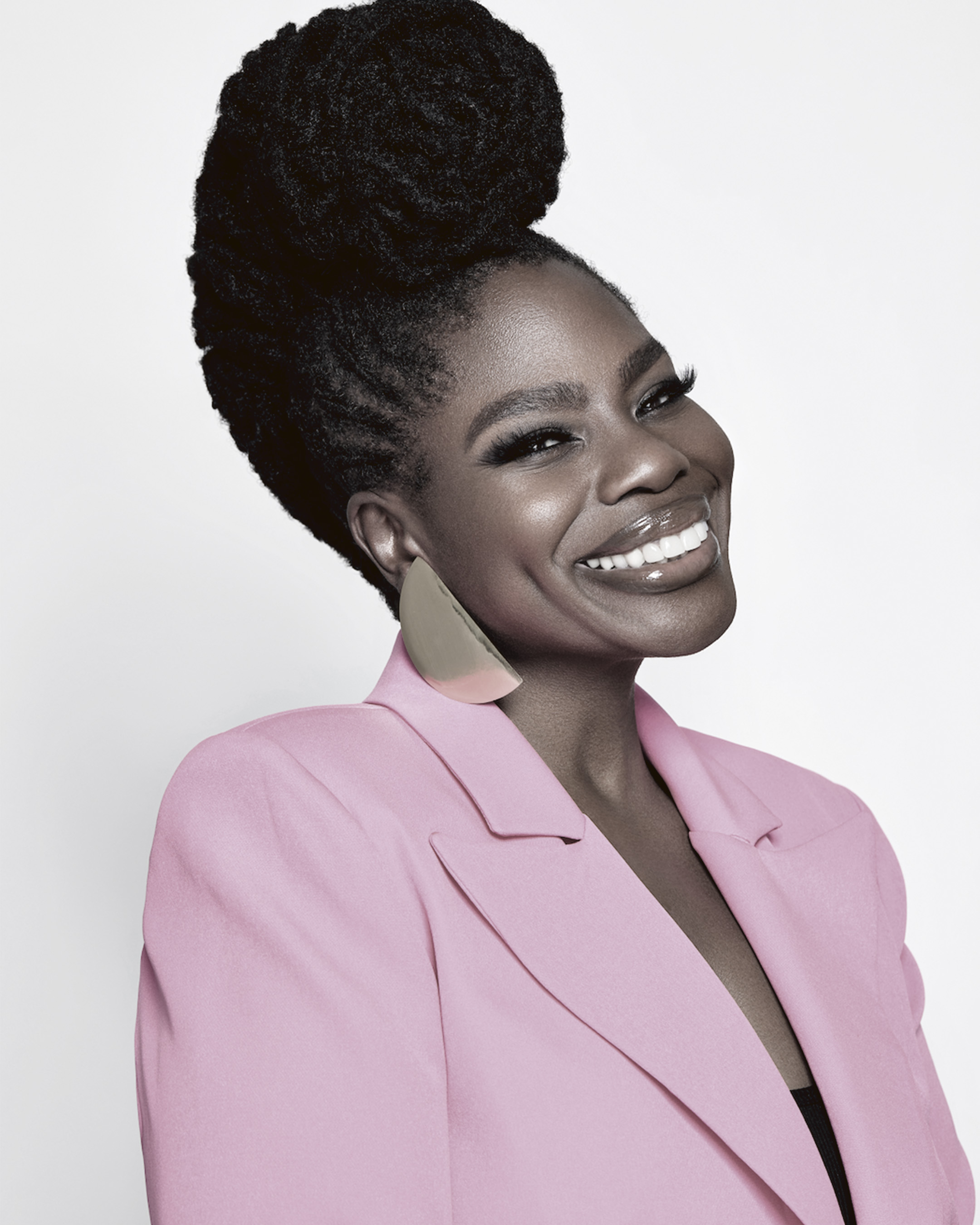 Danessa Myricks smiling, wearing a pink blazer earrings with her hair styled in a high bun.