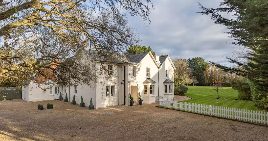 The entrance shows a gravelled driveway and white home overlooking gardens