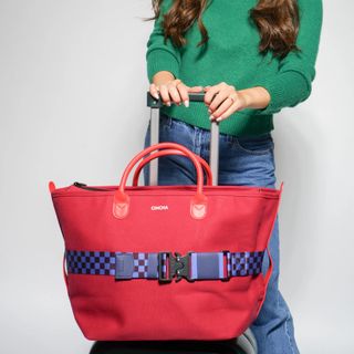 A Cincha travel belt around a red bag on top of a wheeled suitcase