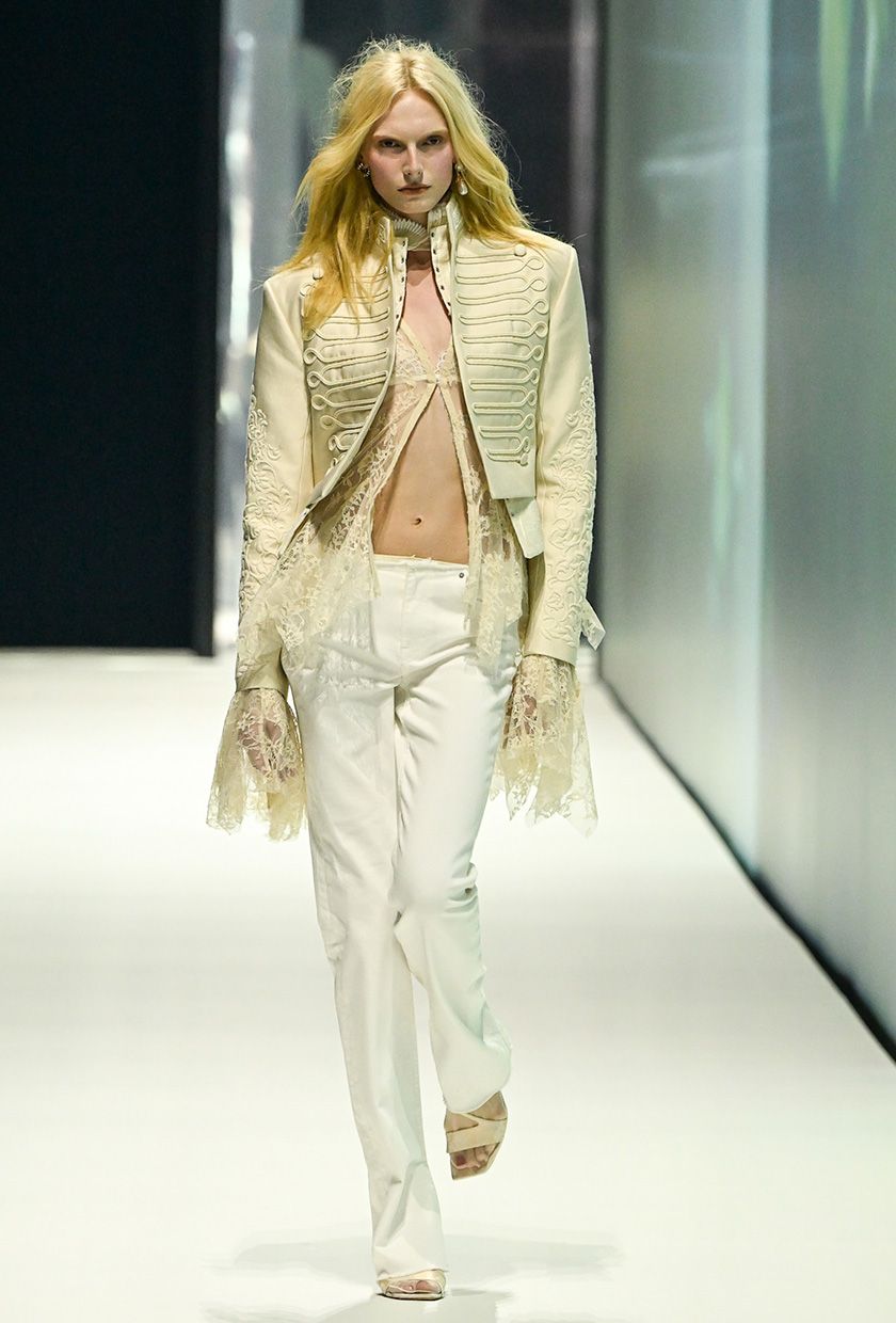H&amp;M model wearing a white jacket over a lace top with white low-rise jeans and white sandals.