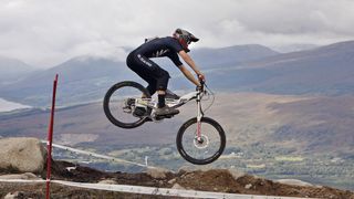Side profile of an intrepid professional mountain biker jumping through the air ahead of the UCI Mountain Bike World Championships 2023.
