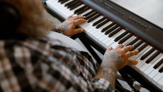 Man sat at keyboard with tattooed hands on the keys