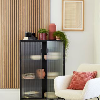 Wooden wall panel in front of black glass fronted cabinet and white armchair