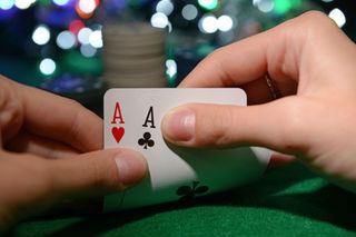 Two hands fold back a pair of playing cards to reveal Aces.