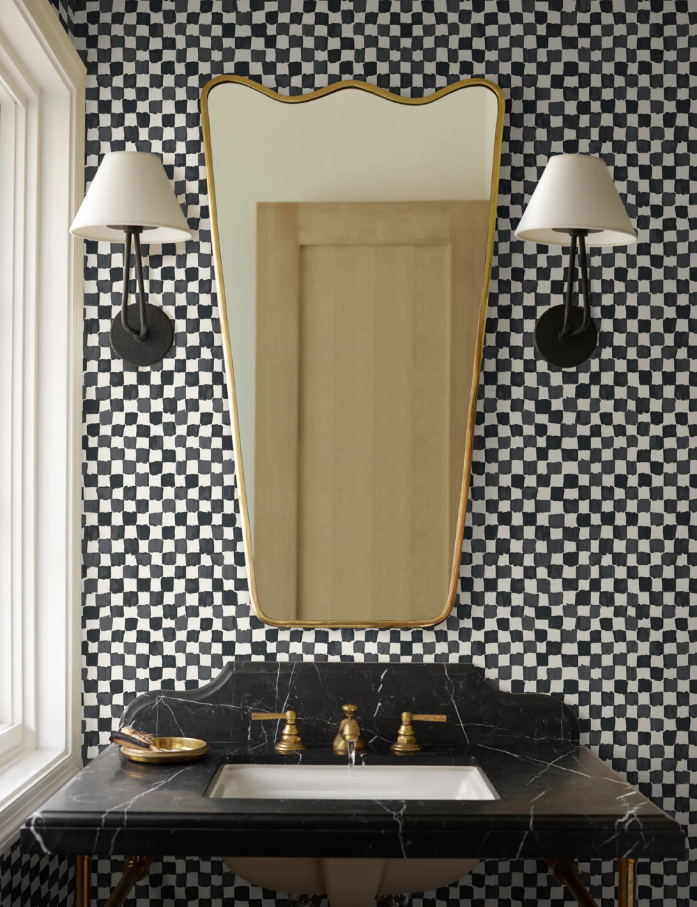 Wavy brass bathroom vanity mirror from Lulu and Georgia's Sarah Sherman Samuel collab hanging above a black marble sink