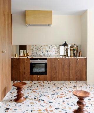 A brown wood kitchen with terrazzo backsplash and floor with vintage hood and stools