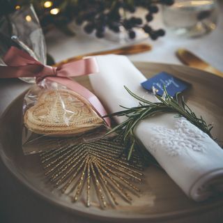 A dining table set for a Christmas dinner with a plate displaying a rolled up embroidered napkin and table favours