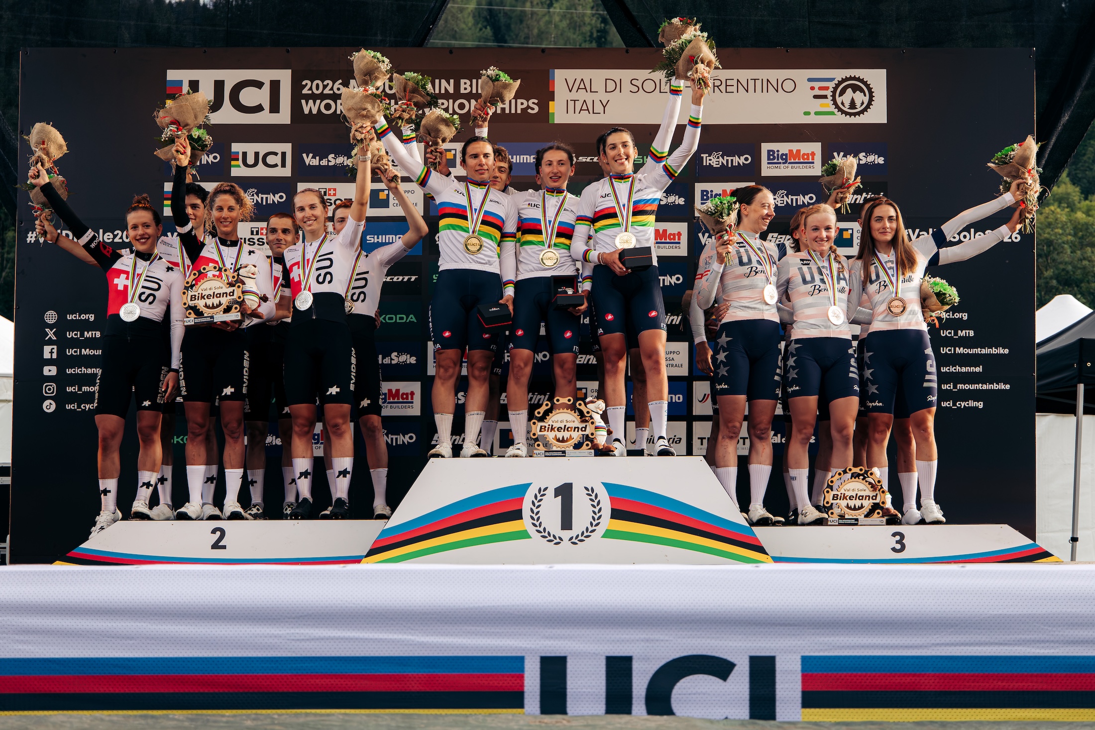Switzerland, winner Italy, and third-place finisher United of States celebrate on the podium following the Team Relay at the 2026 UCI Mountain Bike World Championships in Val di Sole, Italy.