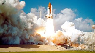 We see the space shuttle Challenger blasting off in a big cloud against a blue sky.