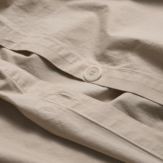 A close up of the button up bottom of a set of cotton bedding in a light biscuit color