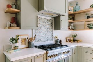 A kitchen with sage green cabinetry and a Moroccan tile oven backsplash