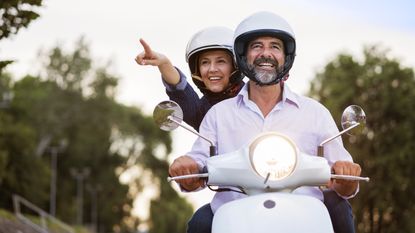 An older couple smiles as they ride a moped.