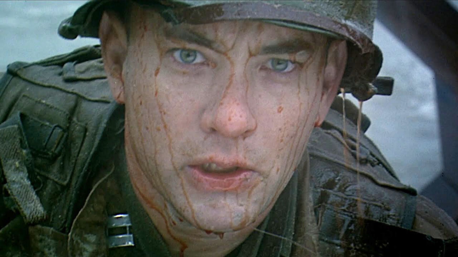 A young Tom Hanks&#039; face is covered in blood stains while wearing an army uniform