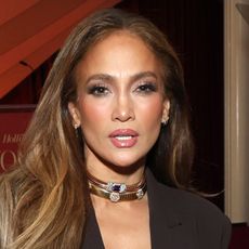 J.lo wears two gold chokers and a brown dress.