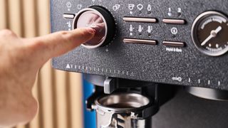 a black espresso machine by kitchenaid photographed against a blue background with silver chrome buttons and a pressure dial and steam wand