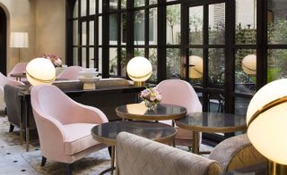 Hotel lounge room with pink chairs, gold and glass tables and floor to ceiling windows