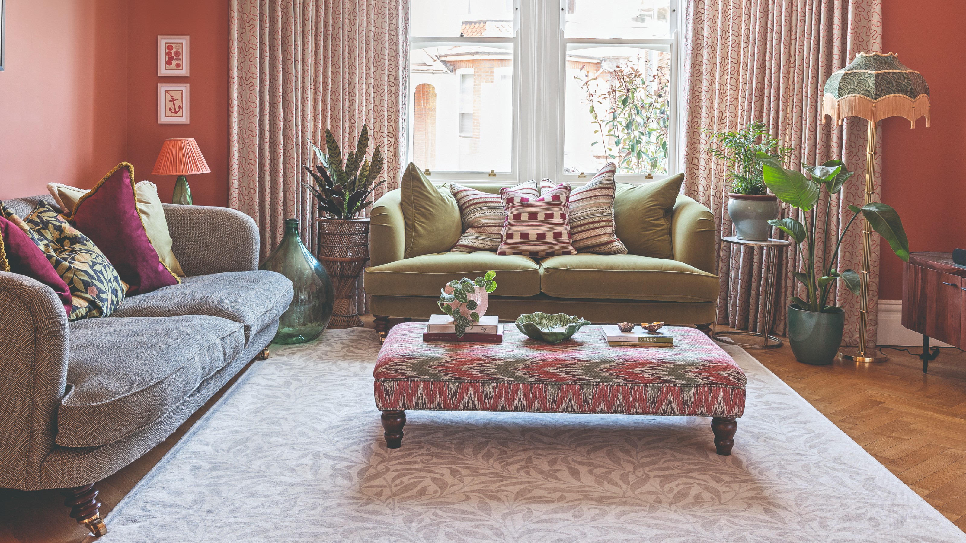 A coral-painted living room with a two sofas, a table lamp with a coral lampshade on a side table and a fringe-trim floor lamp on the other side of the room