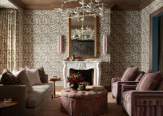 A maximalist living room with drapes with the same pattern as the walls, anchored by an ornate white fireplace. 