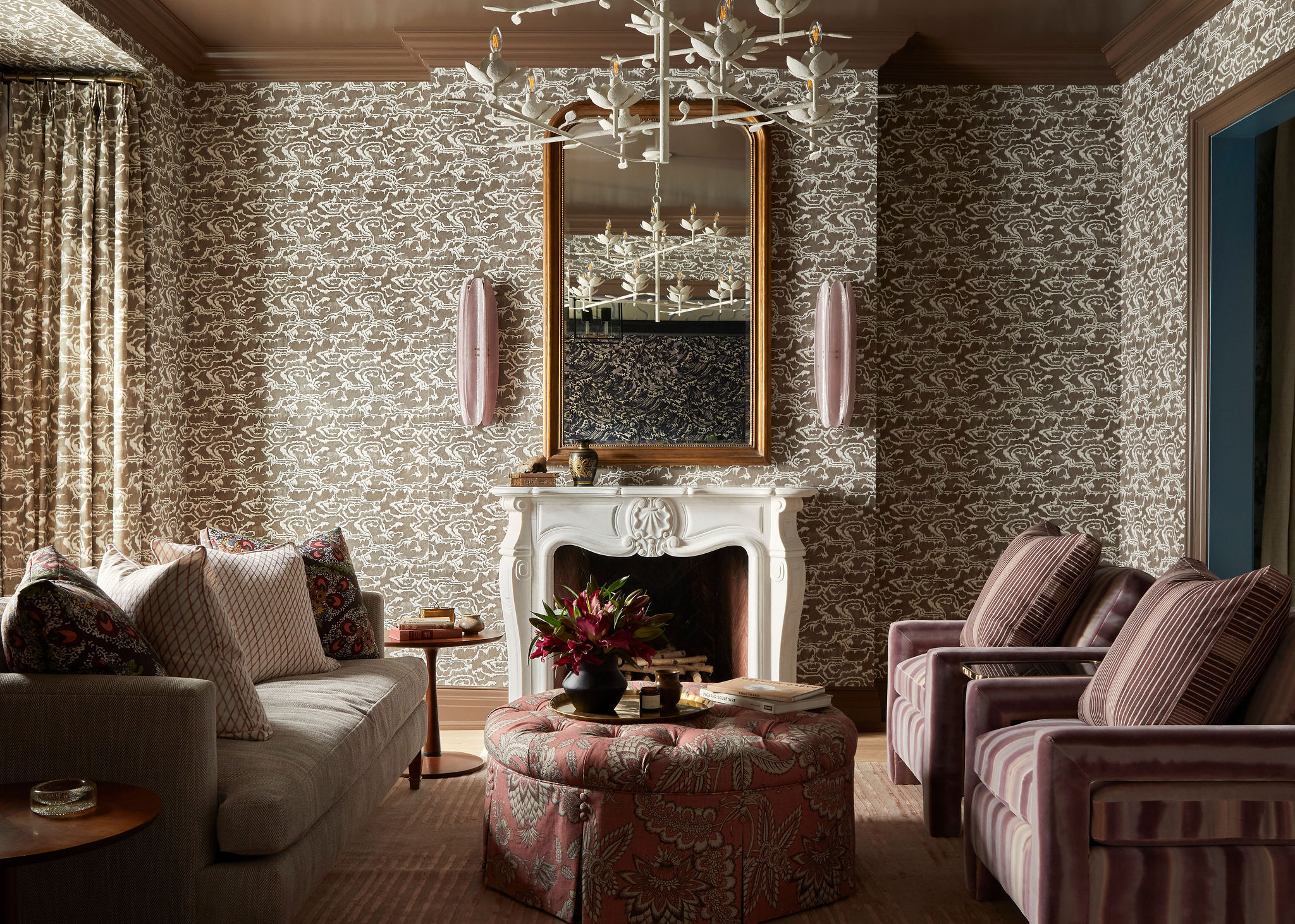 A maximalist living room with drapes with the same pattern as the walls, anchored by an ornate white fireplace. 
