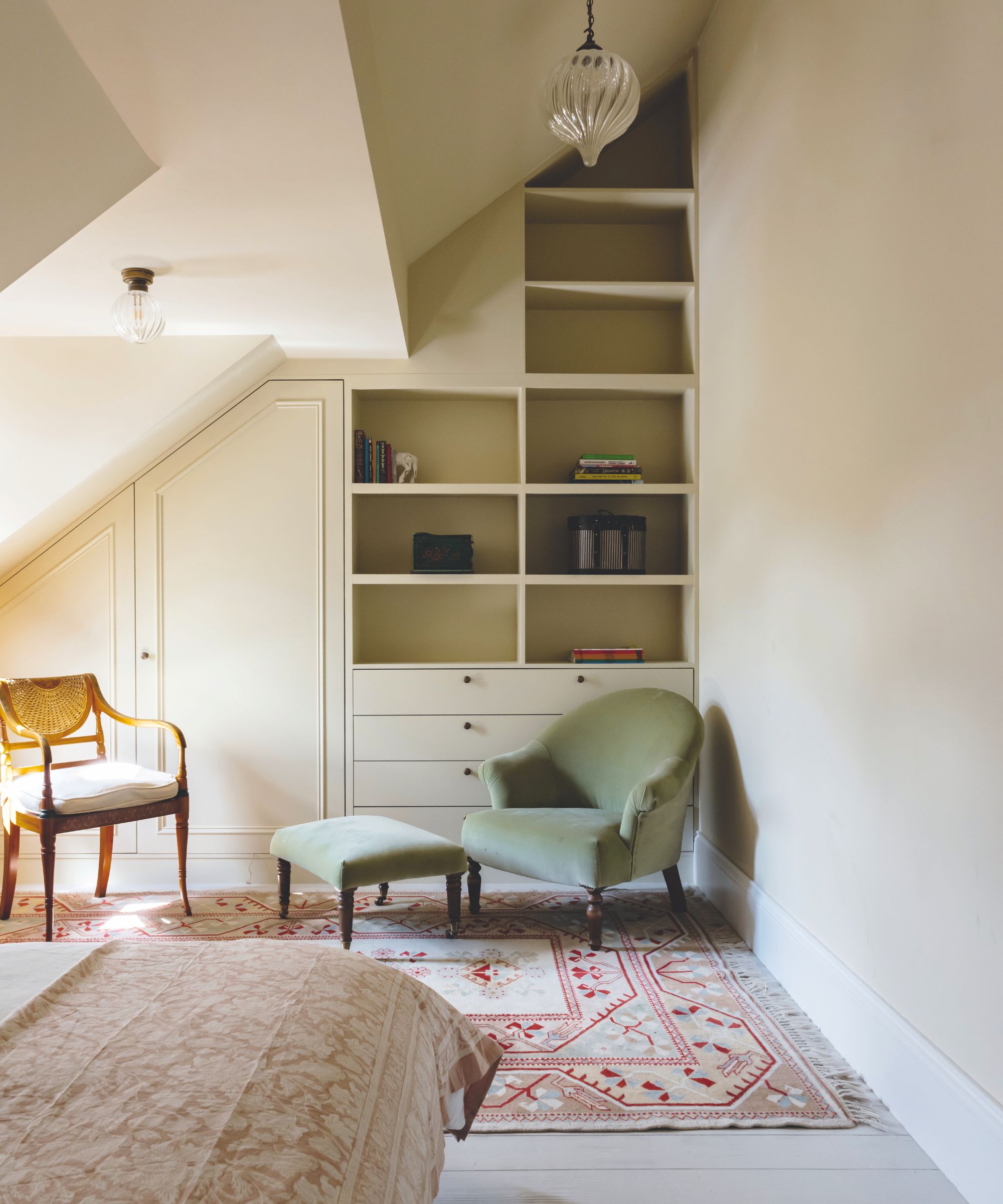 An attic bedroom with built in shelving and cabinets alone the back wall.