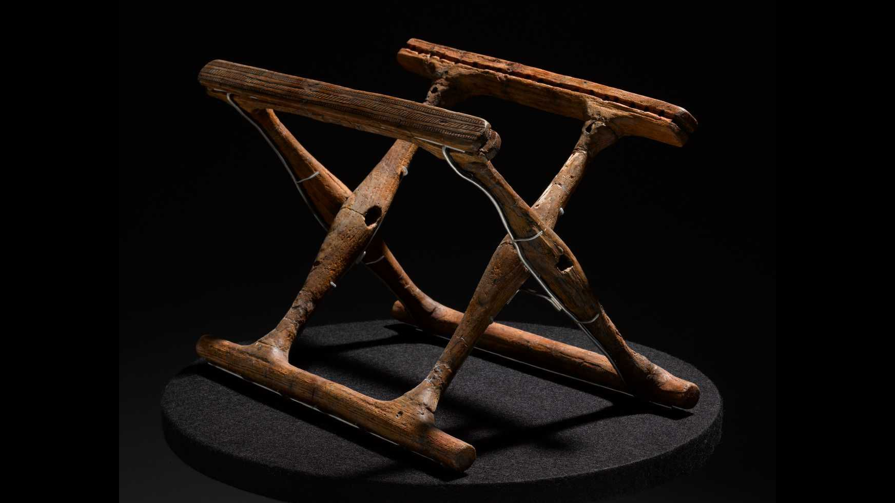 a folding chair base of two wooden squares hitched together at a 45-degree angle against a black background