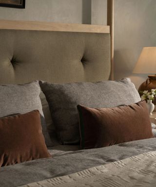 bed with muted blue duvet and pillows, brown velvet decorative pillows and khaki green fabric headboard