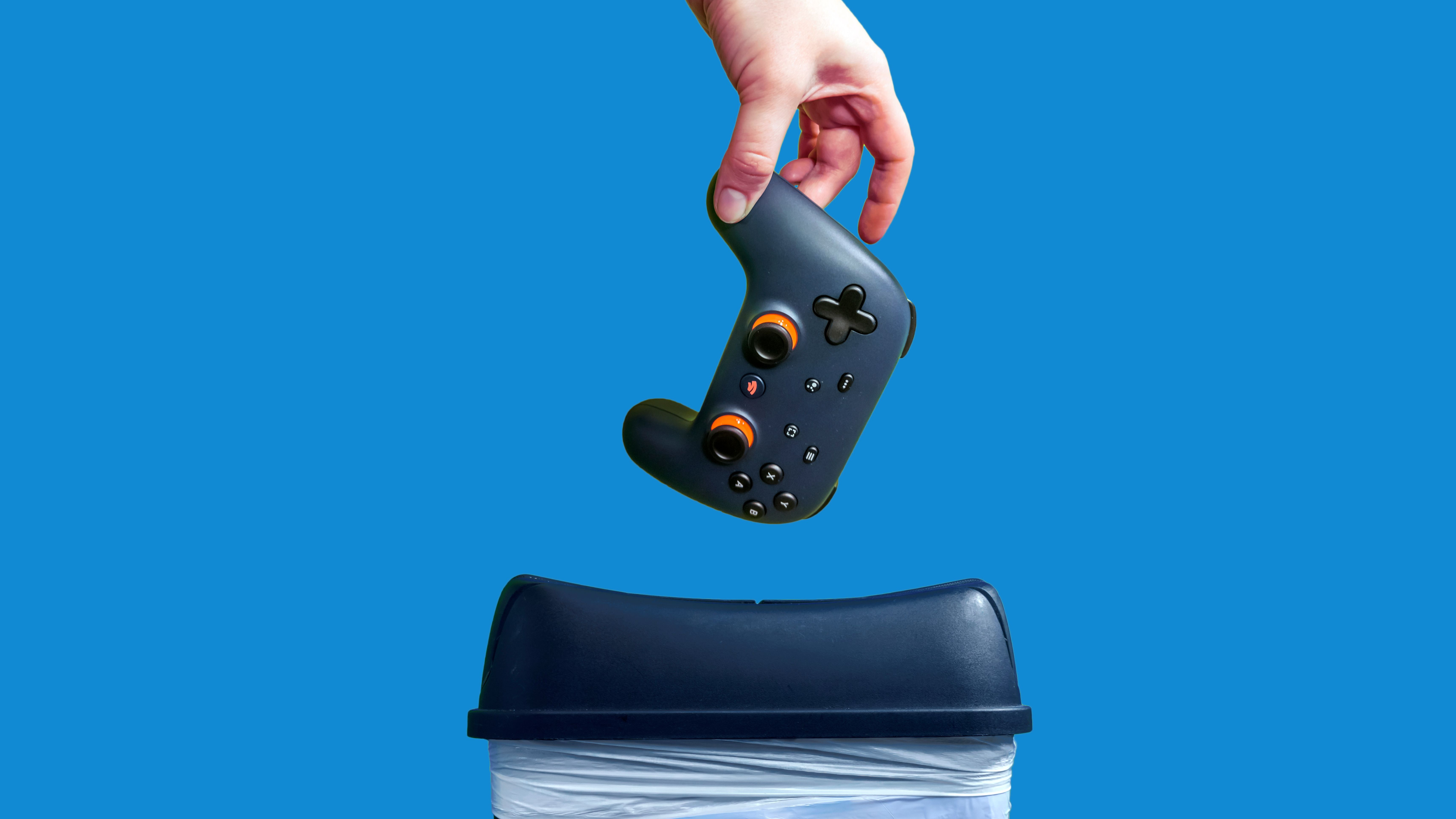 Close-up of a Google Stadia game controller being thrown into the trash in frustration, against a colorful background