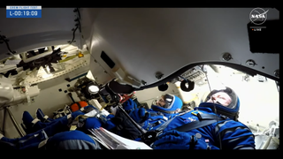 Two astronauts in blue Starliner spacesuits close their helmets for launch