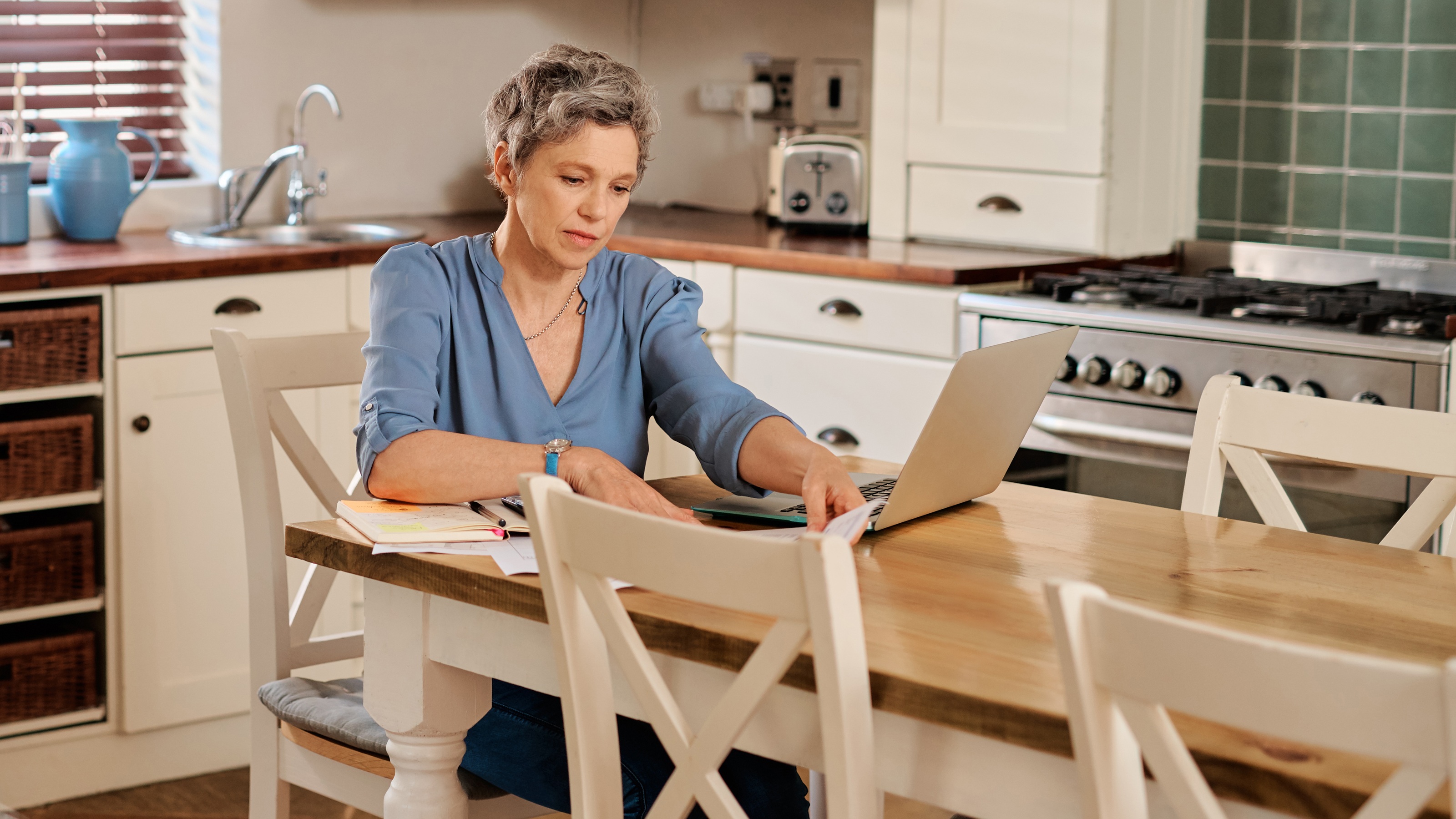 An older woman sits at her kitchen table and works on financial planning.