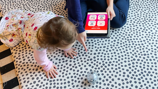 Image of a teenager pointing out a Sphero ball to a crawling toddler on a spotty rug