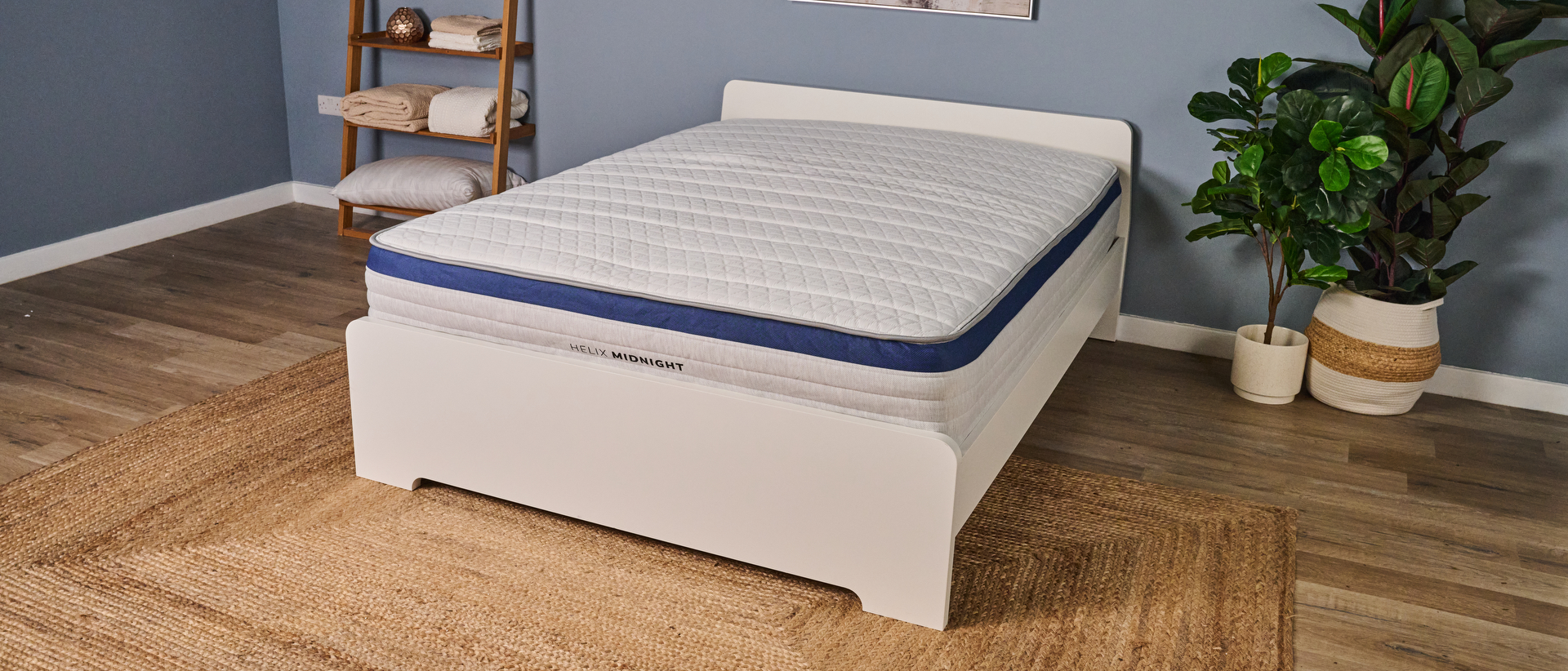 The image shows a white mattress with a royal blue trim on a white bed frame in a blue bedroom