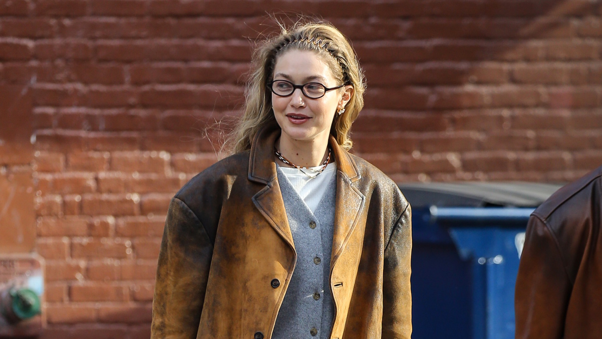 Gigi Hadid wearing a brown leather jacket with a gray cardigan and sweatpants and soft Miu Miu loafers