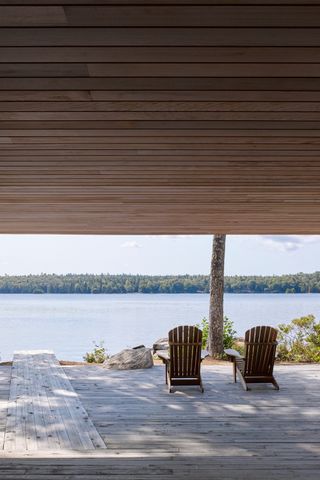 large wooden deck with two adirondack chairs looking out over a lake