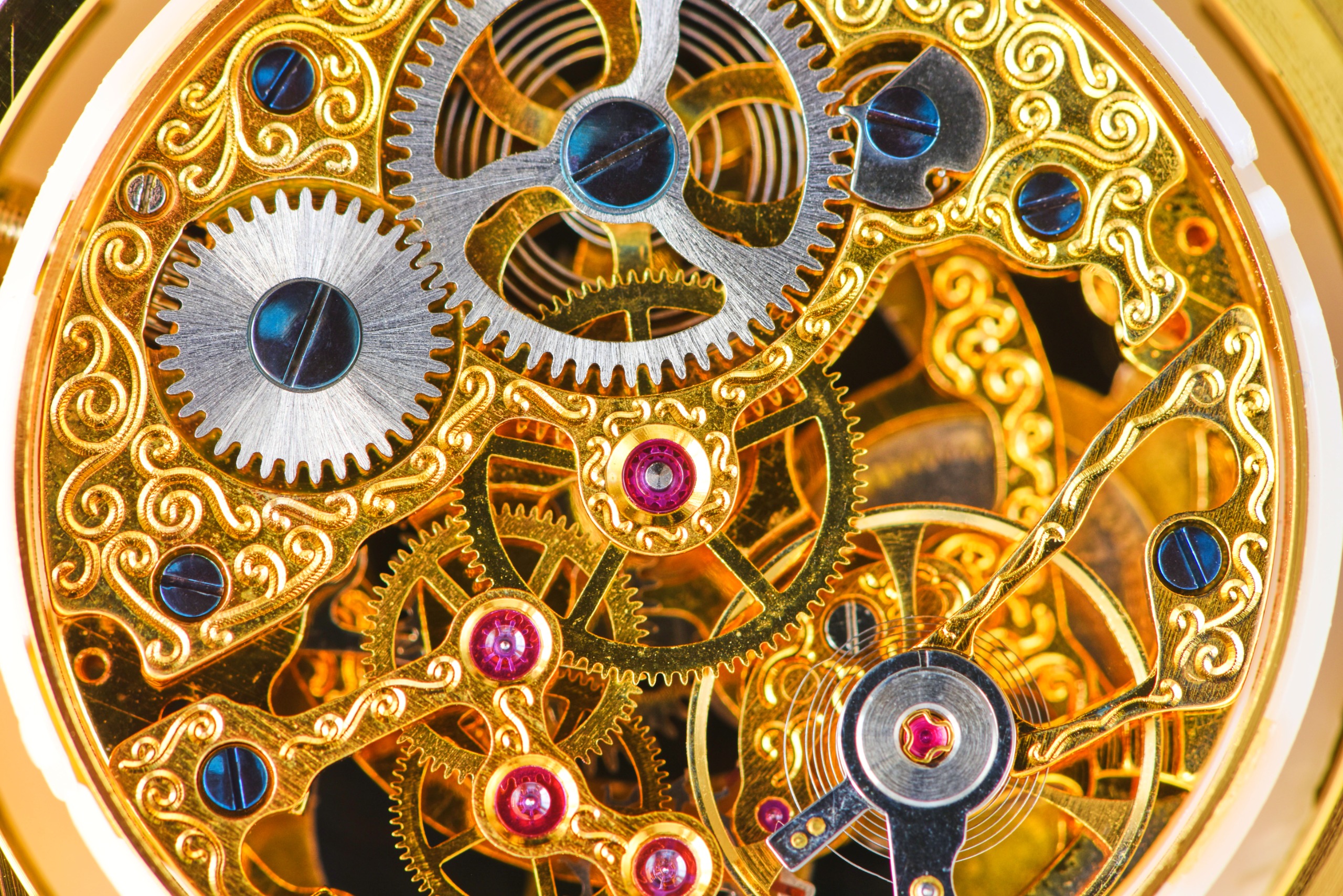 Close-up photograph of the internal components of an Edwardian watch in gold, blue and pink