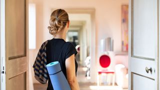 Woman walking into Pilates studio with yoga mat slung over her shoulder, representing wall Pilates