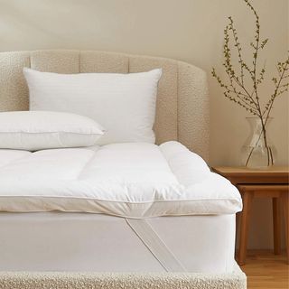 A mattress topper on top of a mattress on a cream boucle bed frame