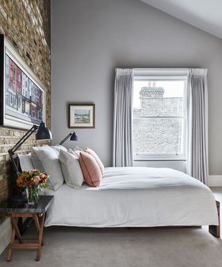 An exposed brick bedroom accent wall in a pale gray scheme with white bedlinen and black anglepoise lamps either side of the bed.