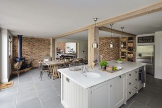 grey open plan kitchen and dining area with exposed brick and corner log burner