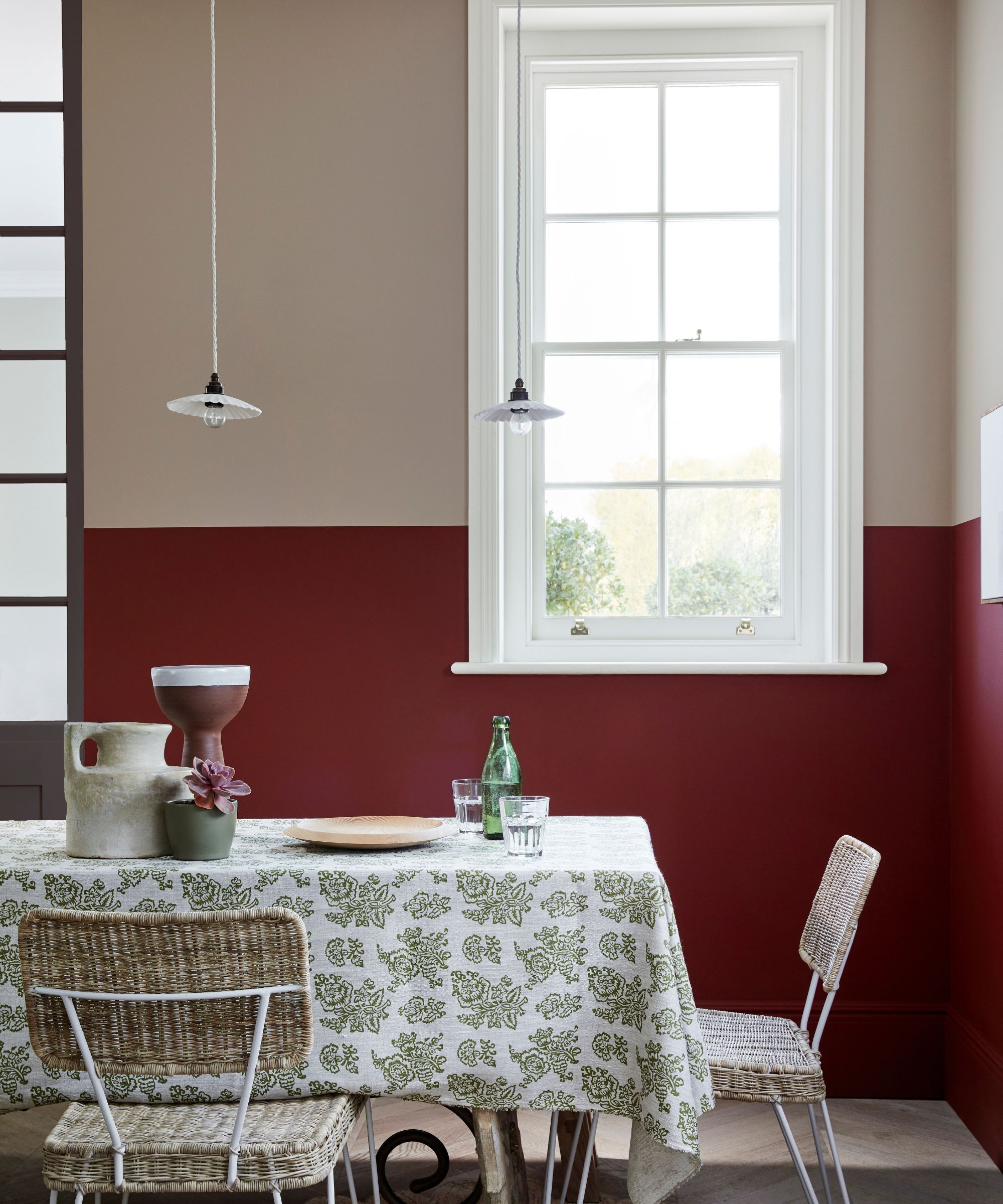 dining room with dark red lower half of wall and beige upper half with large window and dining table with patterned tablecloth
