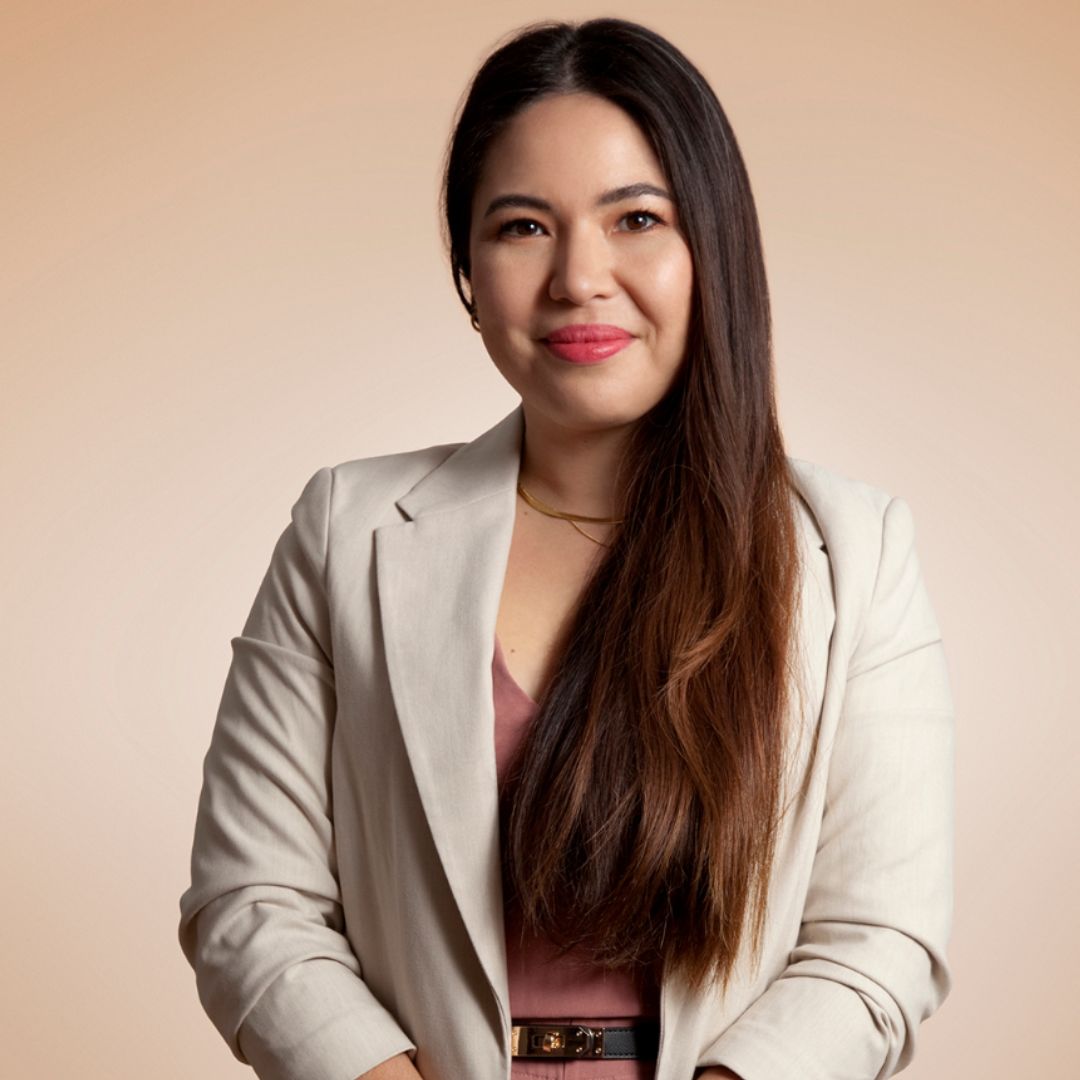Dr. Maria Knöbel headshot. She is wearing a beige blazer standing in front of coral background