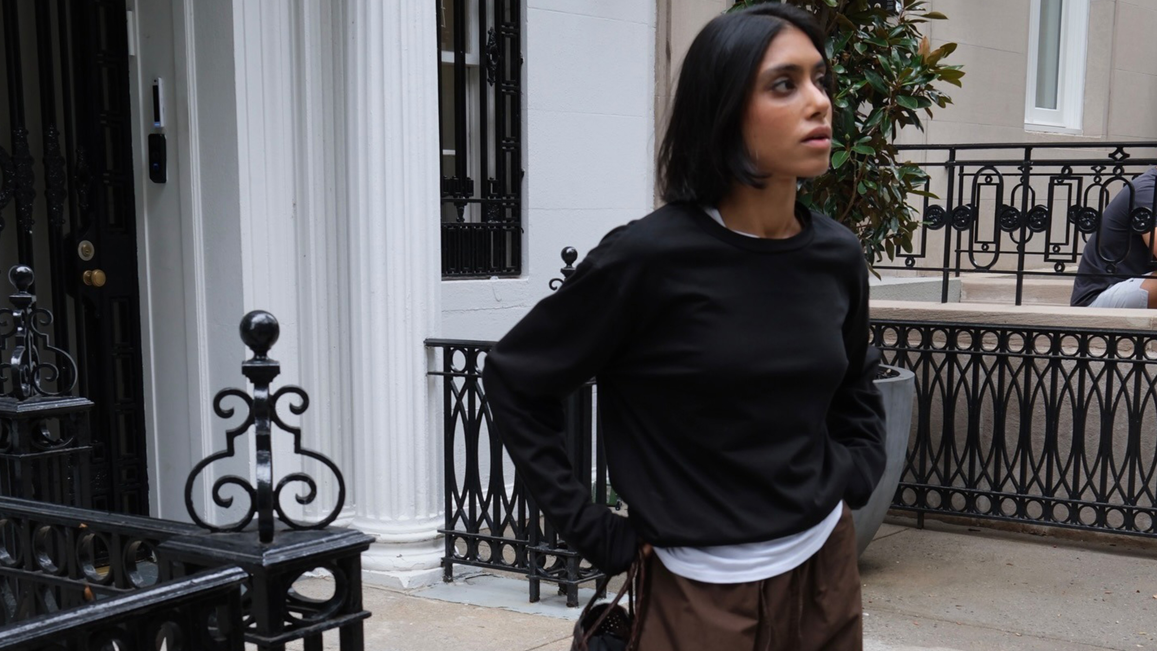 Shay wears a black sweater with a white shirt and brown pants.