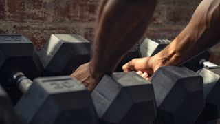 Hands picking up heavy dumbbells from rack