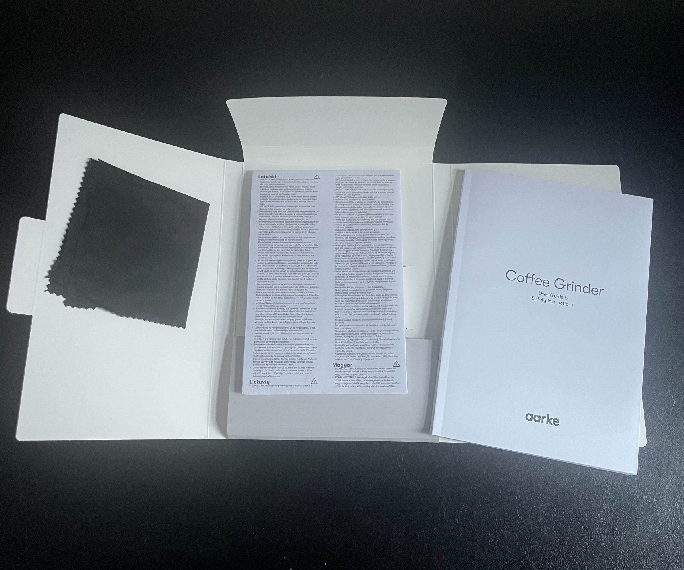 An open white envelope with the Aarke coffee grinder instruction booklet, cloth, and warranty information on top.