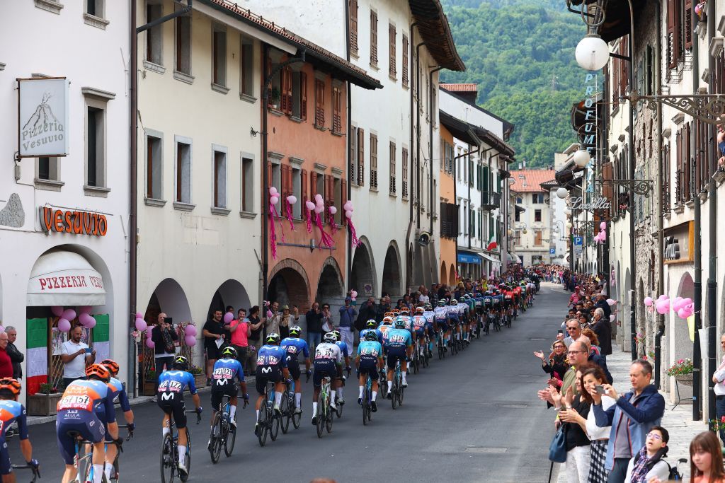 The pack rides through the town of Tolmezzo during the 19th stage of the 107th Giro d'Italia cycling race, 157km between Mortegliano and Sappada on May 24, 2024. (Photo by Luca Bettini / AFP)