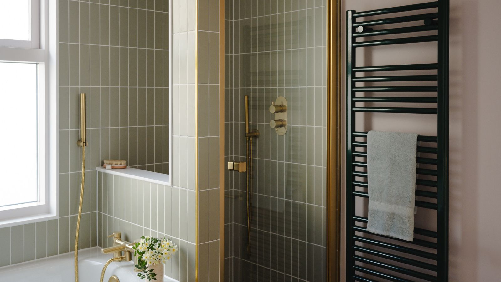 A bathroom with a green-tiled freestanding shower, beside a bathtub. A black wall mounted towel radiator beside the glass shower door. 