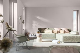 A living room with pale pink walls, a modular pale green sofa, and a modern arm chair