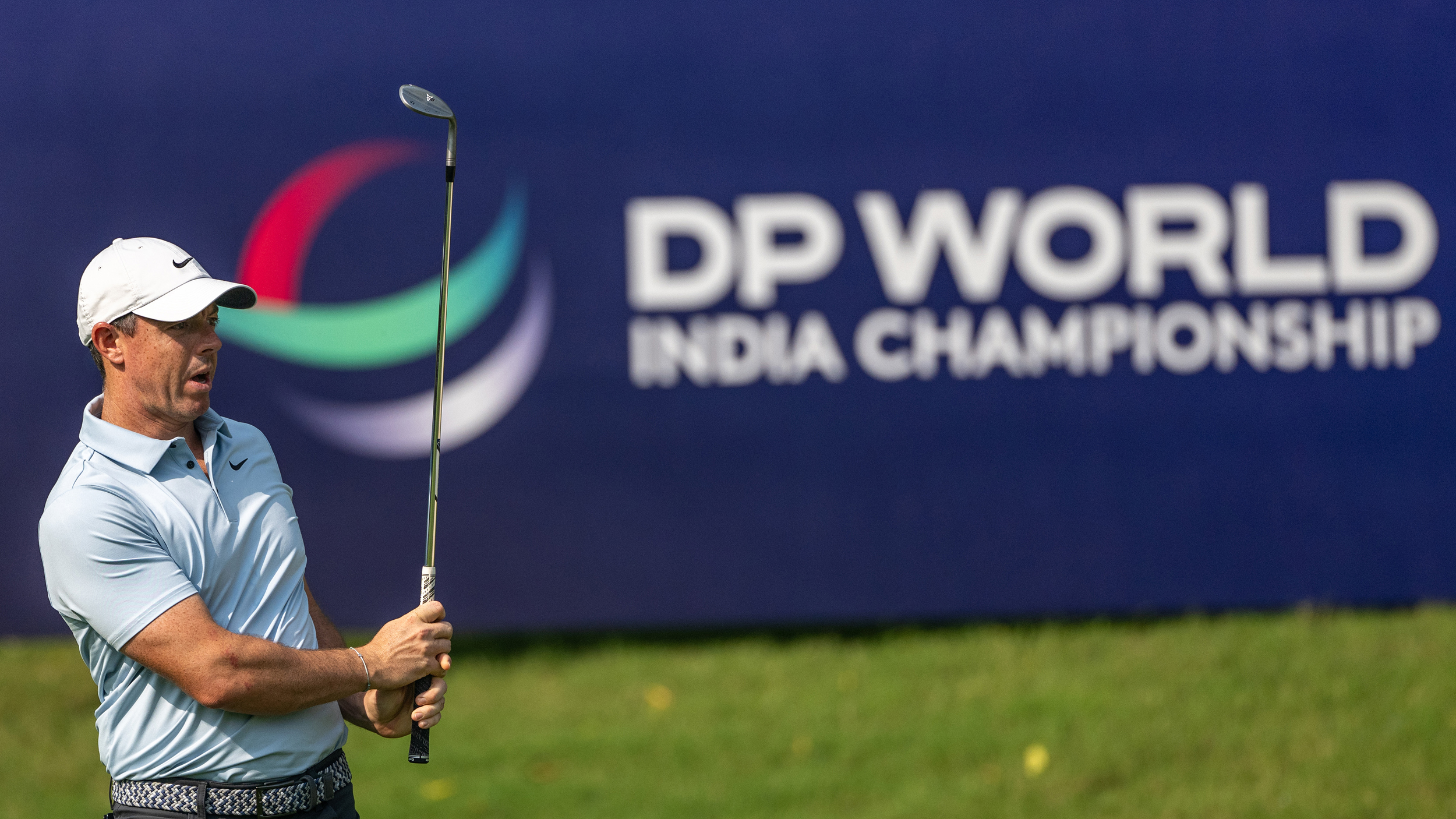 Rory McIlroy looks after a wedge shot with a DP World India Championship sign in the background